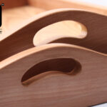 Close-up of two stacked wooden trays with curved handles.