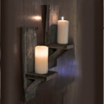 Two wooden wall candle holders with lit candles mounted on a dark wall.