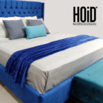 Blue fleece throw on a bed with a tufted blue headboard and decorative pillows.