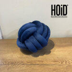 Blue knotted pillow made of suede fabric placed on a wooden surface.
